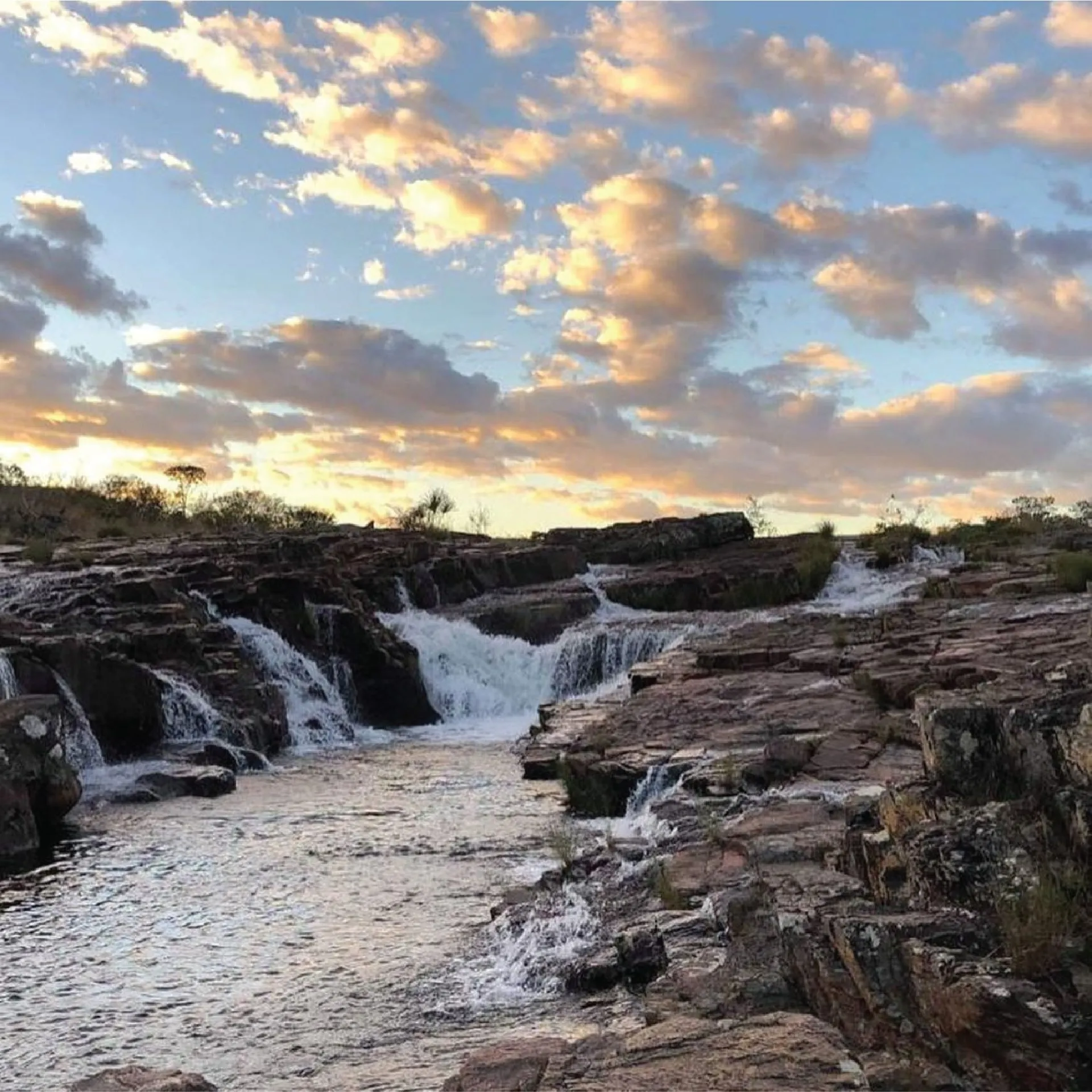 Cachoeira do Papagaio ao entardecer com nuvens douradas refletindo nas águas sobre as rochas